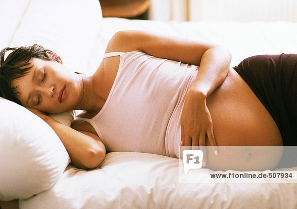 Schwangere Frau mit geschlossenen Augen  seitlich auf dem Bett liegend
