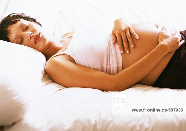 Schwangere Frau mit geschlossenen Augen  die auf dem Rücken auf dem Bett liegt.