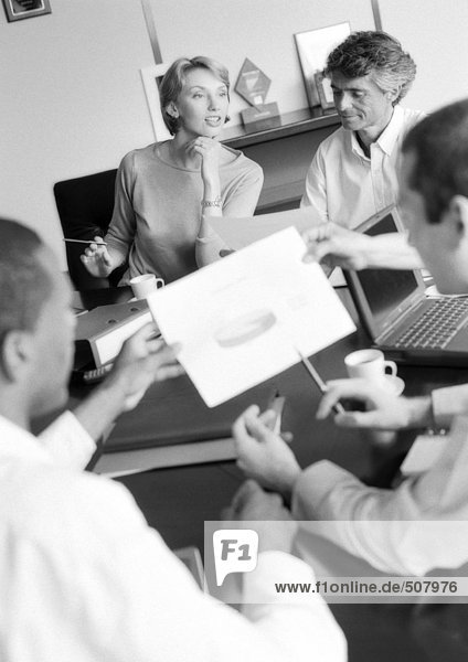 Businesspeople in conference examining document  blurred foreground  B&W