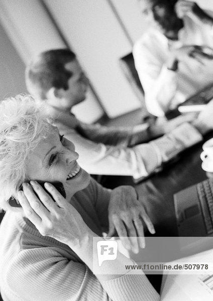 Businesswoman using cell phone in conference room  colleagues in blurred background  B&W