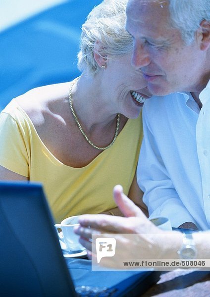 Mature woman and man sitting outdoors with laptop computer