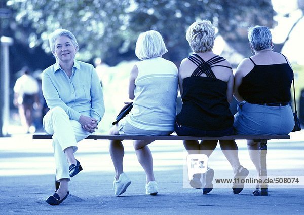 Vier Frauen sitzen auf einer Bank  drei von hinten gesehen