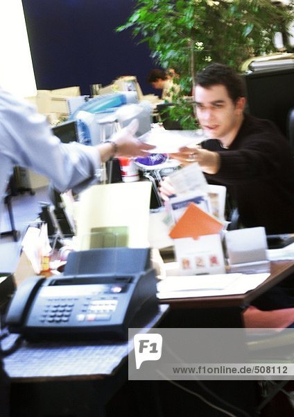 In office  man handing document to second person  blurred