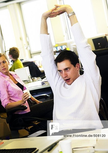 Man stretching in office  colleagues in background