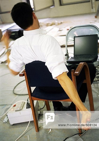 Man sitting in chair stretching arms  in front of laptop computer on chair