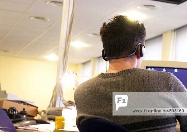 Man wearing headphones and sitting at computer  rear view