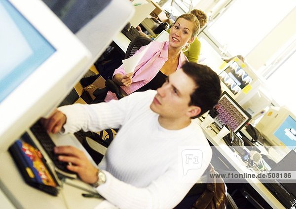 Woman smiling  man working on computer in office