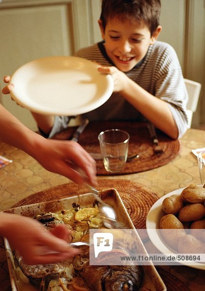 Child at table  holding plate  mother's hands serving food