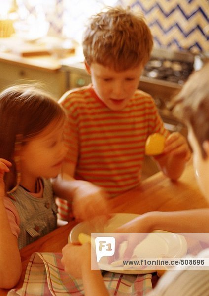Kinder in der Küche legen Apfelscheiben auf Teller  verwischt