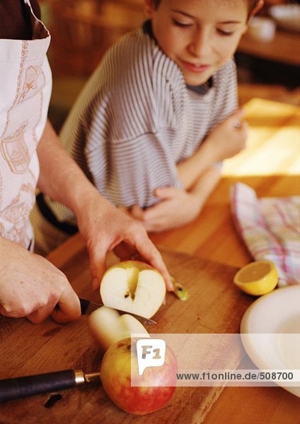 Hände schneiden Äpfel  Kind lehnt sich an die Theke und schaut zu.