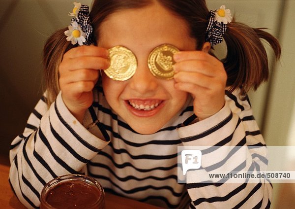 Kind hält Goldmünzen vor den Augen  lächelnd