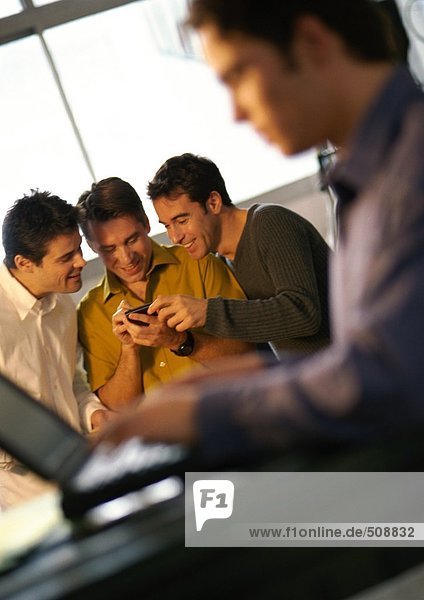 Drei Männer schauen auf Handheld-Computer  vierter Mann mit Laptop im Vordergrund