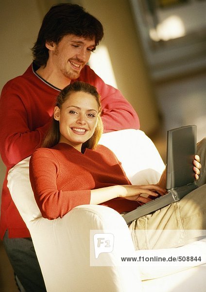 Frau sitzend mit Laptop auf Knien  Mann schaut über die Schulter