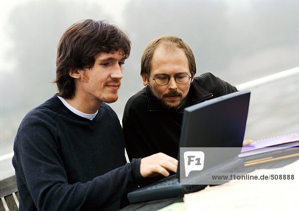 Zwei Männer arbeiten im Freien am Laptop.
