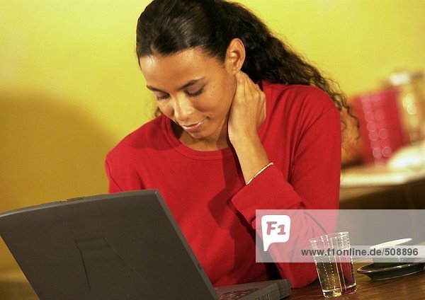 Frau bei der Arbeit am Laptop mit Hand am Hals