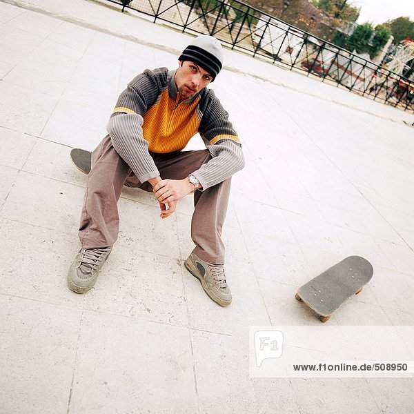 Junger Mann auf dem Skateboard sitzend