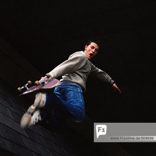 Junger Mann in der Luft hält Skateboard