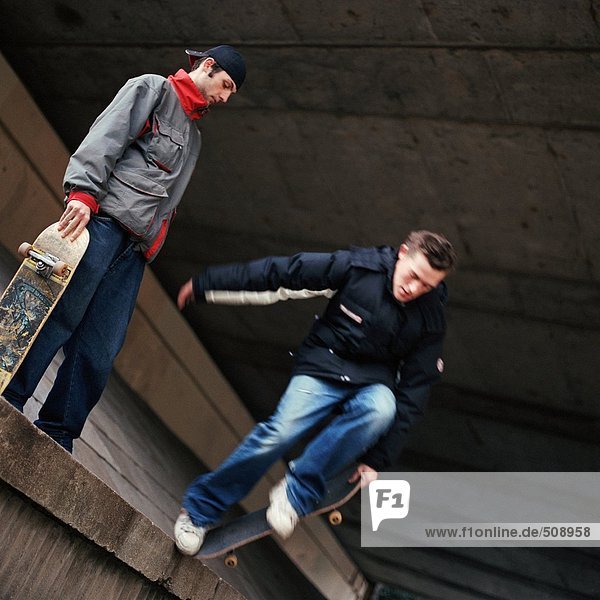Zwei Teenager mit Skateboard  einer springt von der Wand herunter.