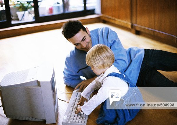 Mann auf dem Boden liegend  Kind vor dem Computer
