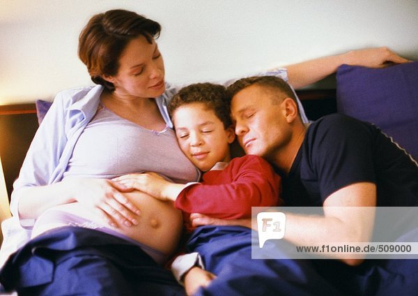 Schwangere Frau sitzend mit Mann und Kind im Bett