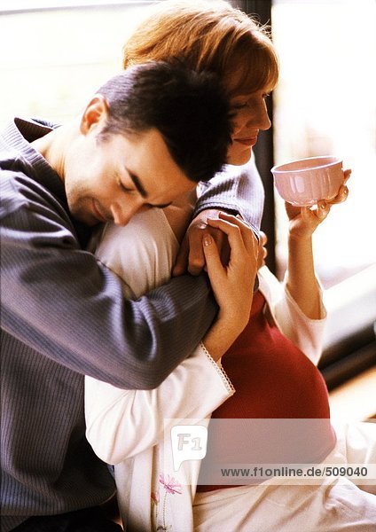 Mann umarmt schwangere Frau von hinten  Seitenansicht