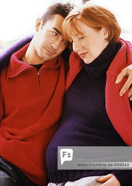 Mann und schwangere Frau sitzend mit Armen umeinander