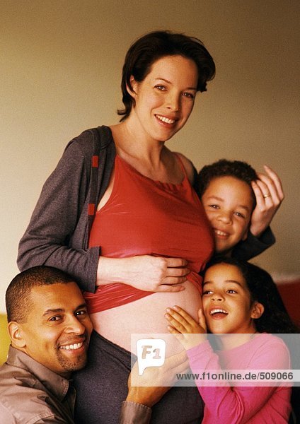 Mann und Kinder um den exponierten Bauch der Schwangeren herum
