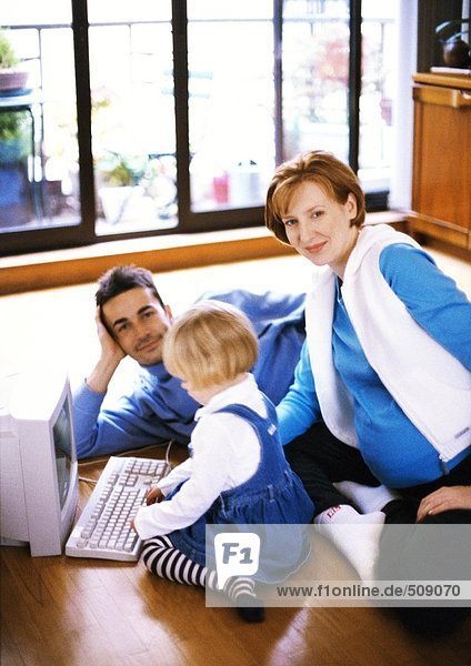 Schwangere Frau und Mann auf dem Boden mit Kind berührt Computer-Tastatur