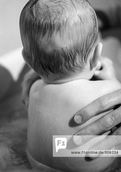 Baby im Bad sitzend  Vaterhand auf dem Rücken  Rückansicht  Nahaufnahme  s/w