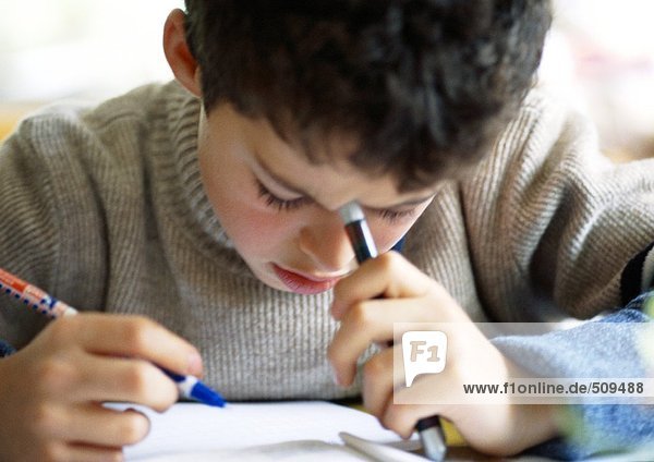 Boy bending head over notebook  writing  close-up