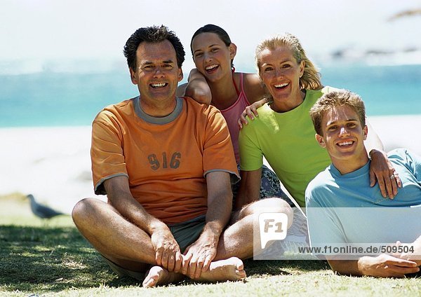Family sitting on beach  smiling  front view  sea in background  portrait.