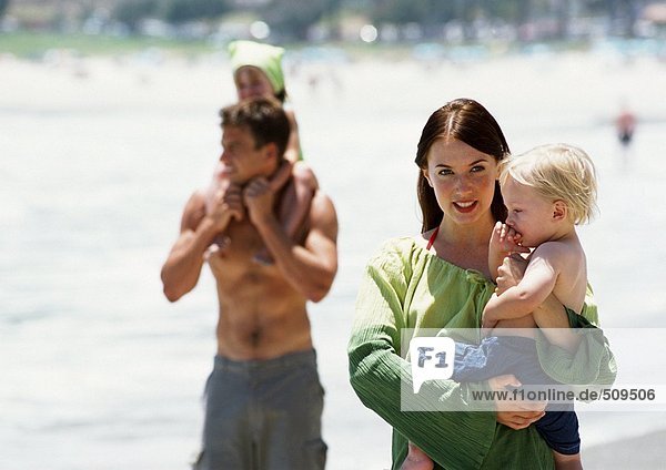 Mann und Frau tragen Kinder am Strand.