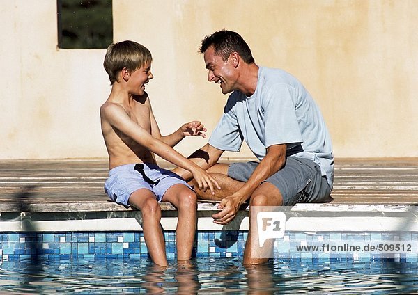 Man and young boy sitting together  feet in pool.
