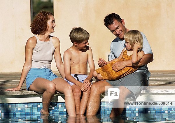 Junge Familie sitzt zusammen  Füße im Pool (Frontalansicht).