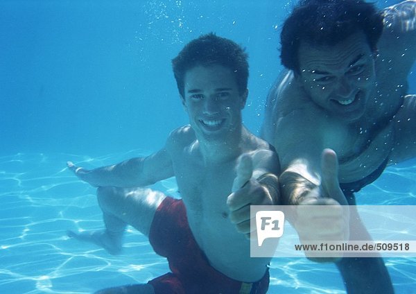 Man and teenage boy underwater making thumbs up sign
