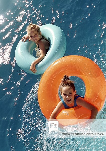 Zwei kleine Mädchen,  die in aufblasbaren Ringen im Wasser schweben,  hohe Winkelansicht