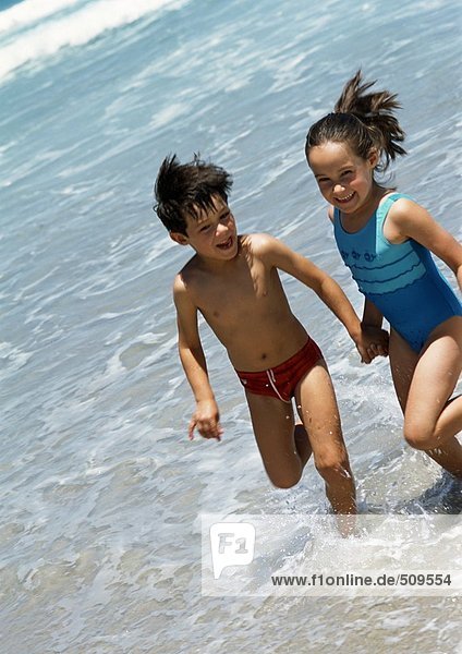 Zwei Kinder halten sich im Wasser am Strand an den Händen.