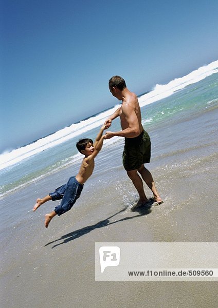 Mann schwingt Kind am Strand.