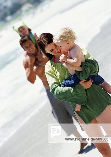 Man and woman holding young children at the beach.