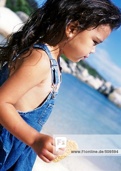Kleines Mädchen hält Snack am Strand  Seitenansicht  Nahaufnahme