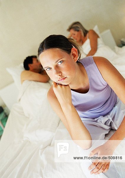 Teenagermädchen auf dem Bett der Eltern sitzend  Eltern im Hintergrund liegend