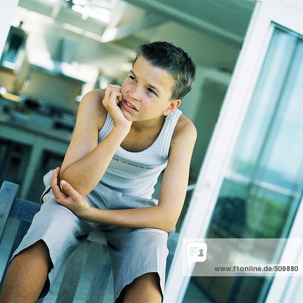 Teenager-Junge sitzend mit der Hand unter dem Kinn