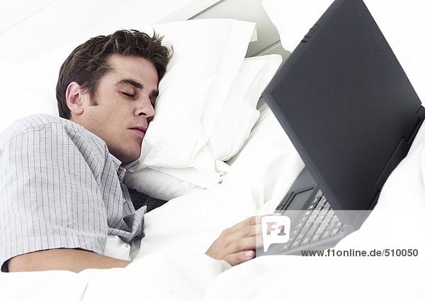 Mann auf dem Bett liegend mit geschlossenen Augen  Hand auf Laptop-Computer