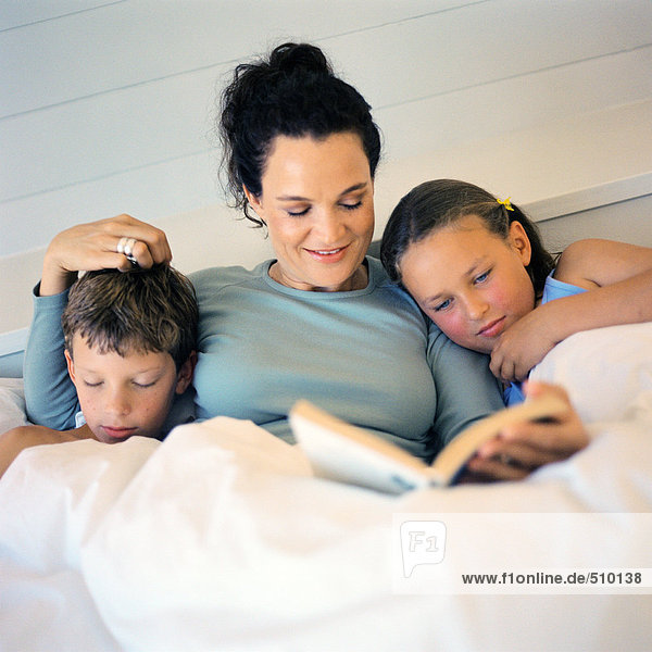 Mother lying in bed between children  reading book