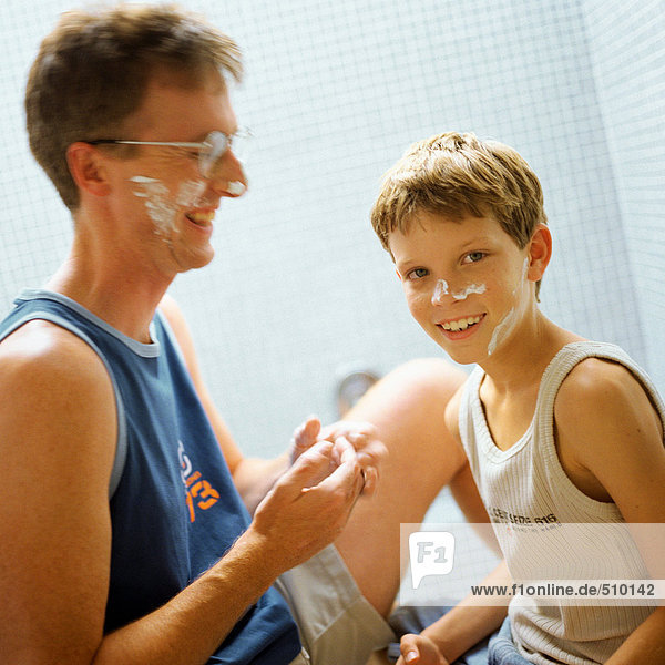 Father and son with shaving cream on faces  smiling