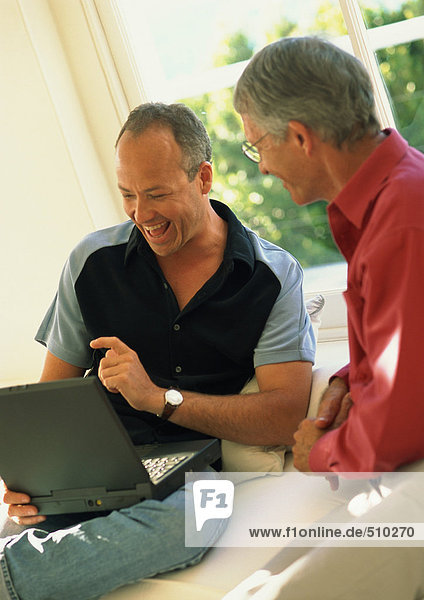 Two men sitting  one using laptop computer