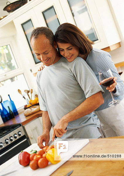 Couple in kitchen  man cutting vegetables while woman looks over man's shoulder