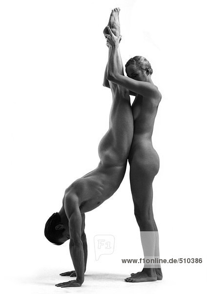 Nude man and woman  man doing handstand  woman holding man's ankles  side view  b&w