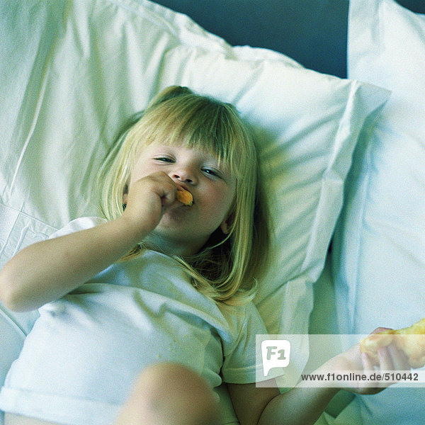 Kind auf dem Bett liegend  essend