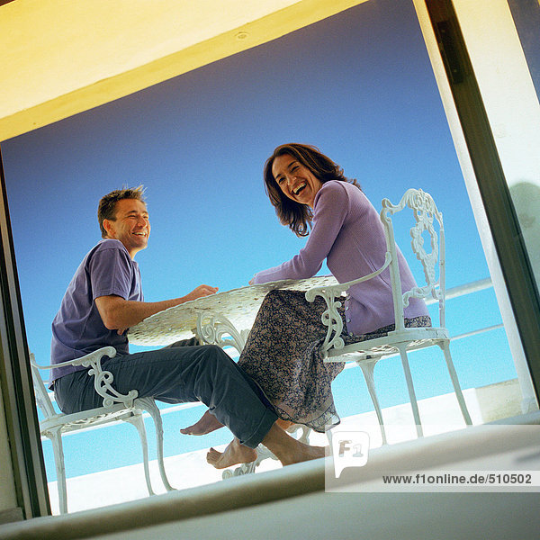 Mann und Frau sitzen am Tisch im Freien  lächelnd  durchs Fenster gesehen  Blickwinkel niedrig